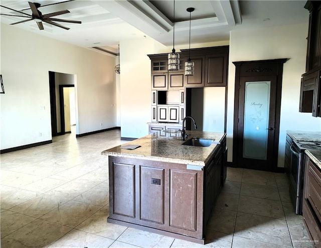 kitchen featuring hanging light fixtures, an island with sink, light stone countertops, and sink