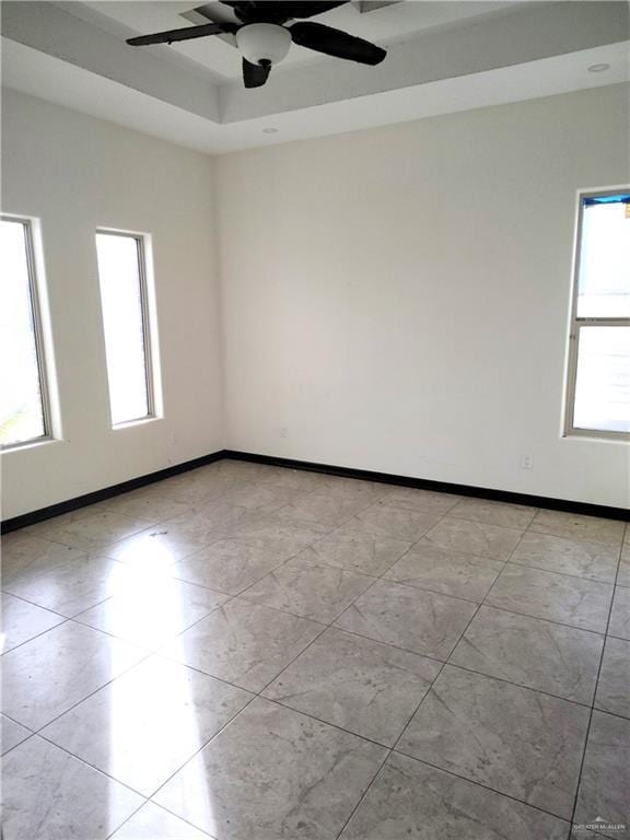 empty room with light tile patterned floors, a wealth of natural light, ceiling fan, and a tray ceiling