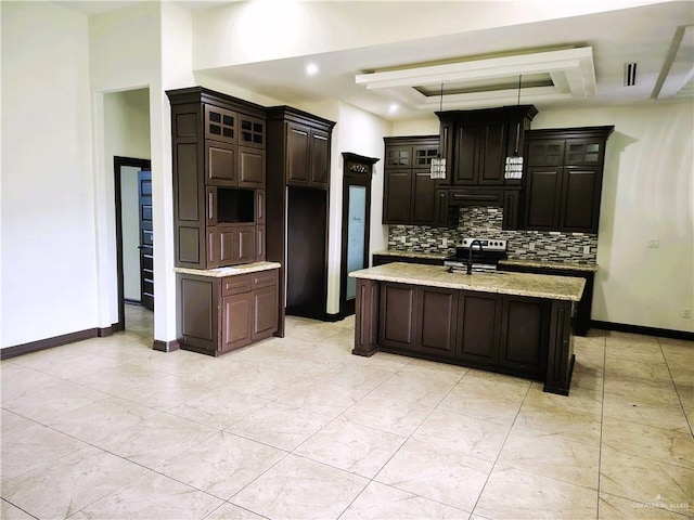 kitchen with stainless steel range with electric stovetop, backsplash, dark brown cabinets, and an island with sink