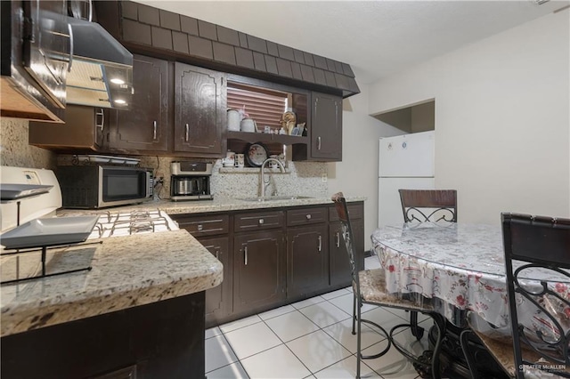 kitchen with dark brown cabinets, white refrigerator, light tile patterned floors, and sink