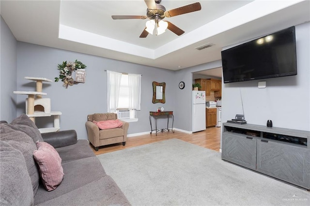 living room with a tray ceiling, ceiling fan, cooling unit, and light wood-type flooring