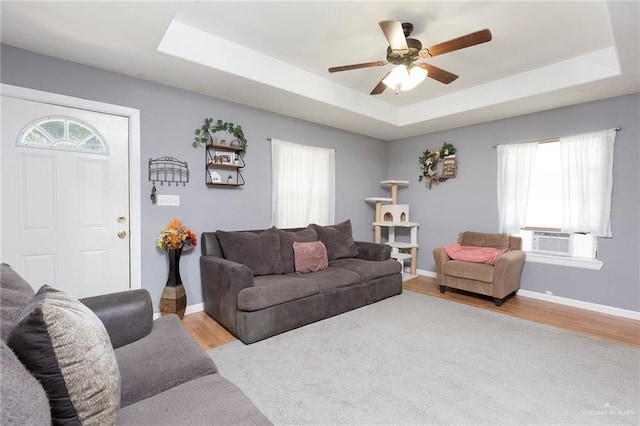 living room featuring cooling unit, light hardwood / wood-style floors, and a tray ceiling