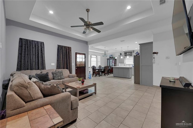 living room featuring a tray ceiling, ceiling fan, and light tile patterned floors