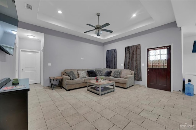 tiled living room featuring ceiling fan and a tray ceiling