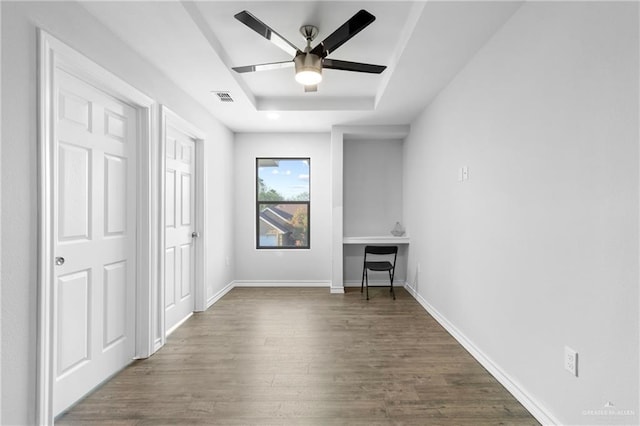 empty room featuring a raised ceiling, ceiling fan, and dark wood-type flooring