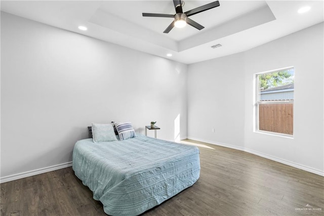 bedroom with ceiling fan, a raised ceiling, and dark wood-type flooring