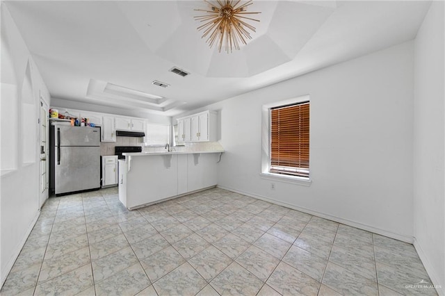 4217 W Ithaca Ave, Mcallen, TX 78501 - kitchen with freestanding refrigerator, a tray ceiling, a peninsula, under cabinet range hood, and white cabinetry