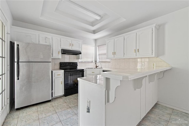 4217 W Ithaca Ave, Mcallen, TX 78501 - kitchen with freestanding refrigerator, black electric range, under cabinet range hood, a peninsula, and a tray ceiling