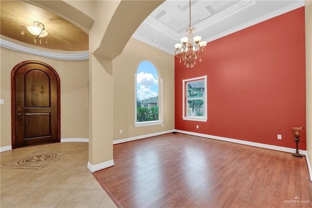 spare room with a raised ceiling, a chandelier, light hardwood / wood-style floors, and ornamental molding