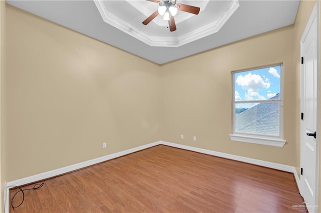 empty room with hardwood / wood-style flooring, ceiling fan, ornamental molding, and a tray ceiling