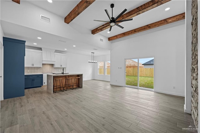 living room with beam ceiling, sink, ceiling fan with notable chandelier, and light hardwood / wood-style flooring