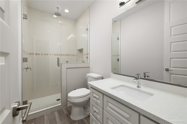 bathroom featuring a stall shower, toilet, vanity, and wood finished floors