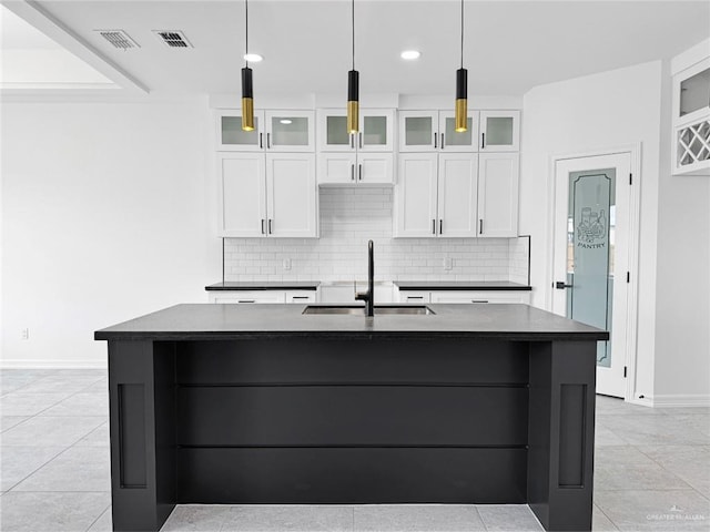 kitchen with a kitchen island with sink, sink, white cabinets, and decorative light fixtures