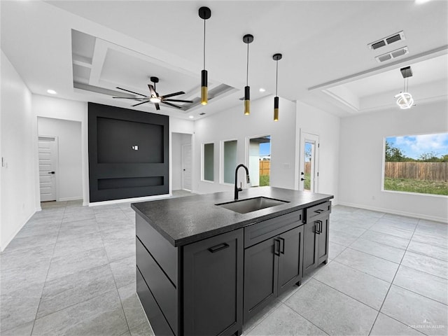 kitchen featuring coffered ceiling, a center island with sink, sink, ceiling fan, and decorative light fixtures