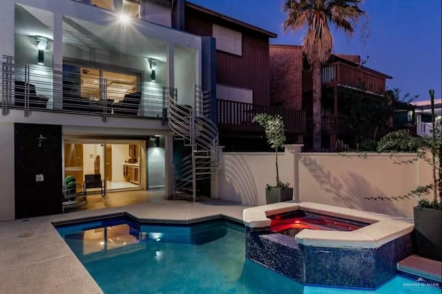 back of house at twilight with a balcony, a patio area, a pool with connected hot tub, and fence