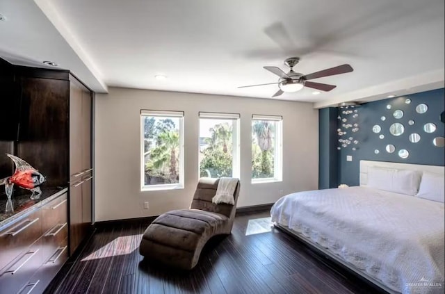 bedroom with dark wood-style floors, ceiling fan, an accent wall, and baseboards