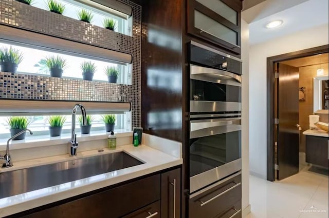 kitchen with dark brown cabinets, stainless steel double oven, a sink, and light countertops