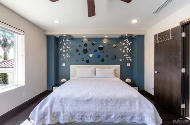 bedroom featuring dark wood-style floors, an accent wall, visible vents, and baseboards