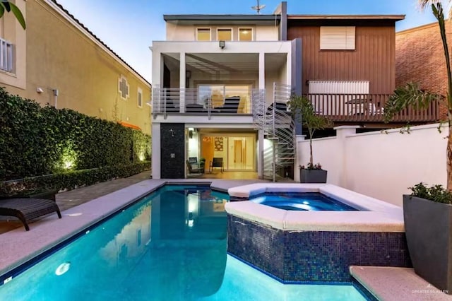 rear view of property featuring a balcony and a pool with connected hot tub