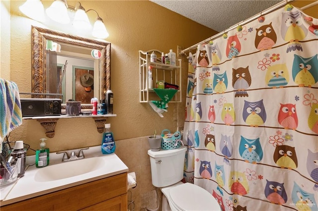 bathroom with a textured ceiling, tile walls, vanity, toilet, and a textured wall