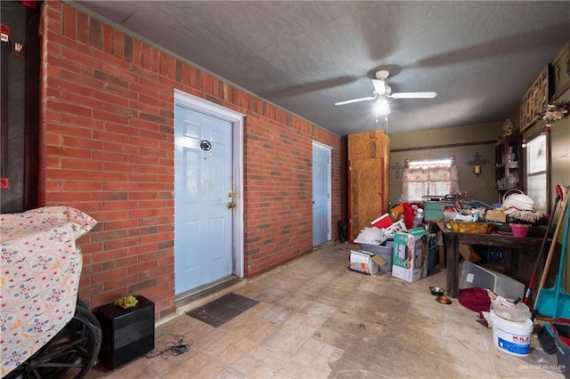 interior space with a ceiling fan and brick wall