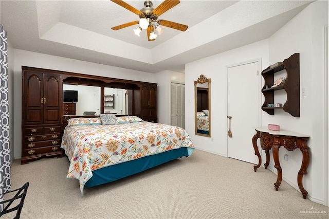 bedroom with ceiling fan, a raised ceiling, a closet, and light carpet