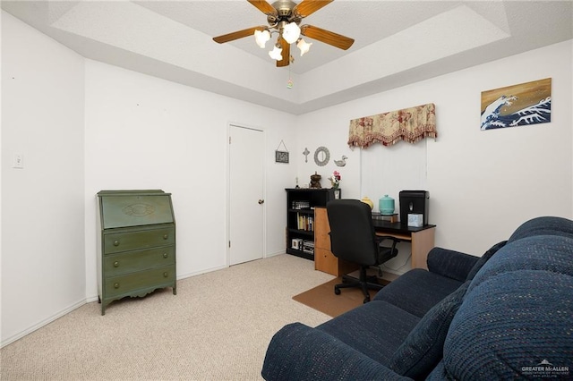 office featuring ceiling fan, light colored carpet, and a raised ceiling