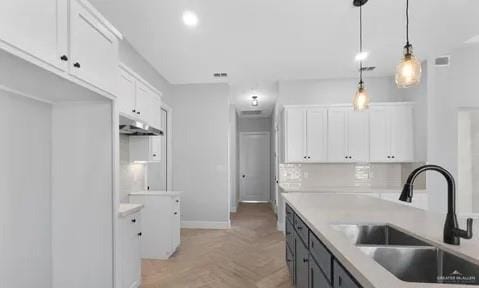 kitchen with under cabinet range hood, pendant lighting, white cabinets, and a sink