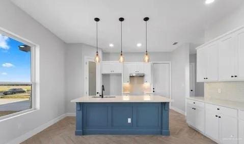 kitchen with baseboards, a kitchen island, white cabinetry, and under cabinet range hood