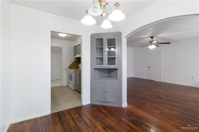 unfurnished dining area featuring ceiling fan with notable chandelier, dark hardwood / wood-style flooring, and ornamental molding