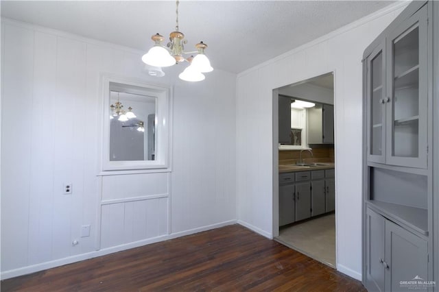 unfurnished dining area featuring sink, ornamental molding, dark hardwood / wood-style floors, and a notable chandelier