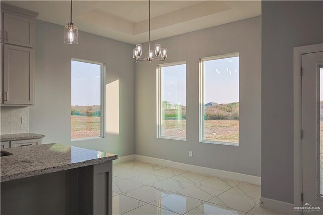 unfurnished dining area with a raised ceiling and a chandelier