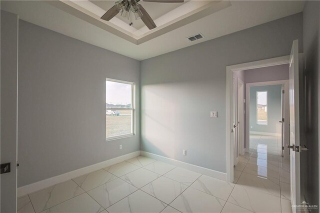 unfurnished room featuring a raised ceiling, ceiling fan, and a healthy amount of sunlight