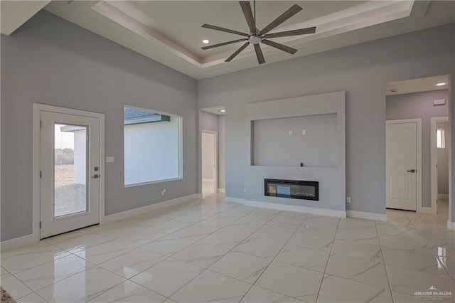 unfurnished living room with ceiling fan and a raised ceiling