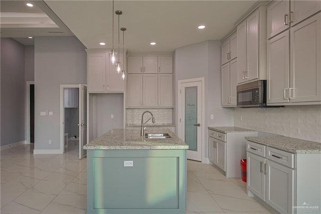 kitchen with backsplash, light stone counters, sink, a center island with sink, and hanging light fixtures