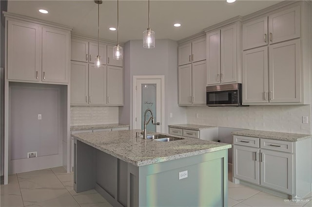 kitchen with a center island with sink, sink, hanging light fixtures, decorative backsplash, and light stone counters