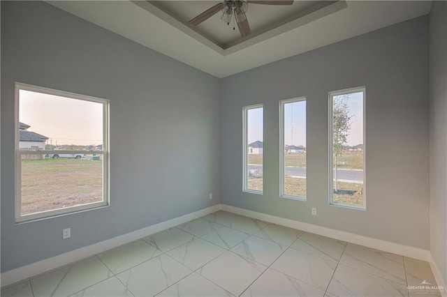 empty room featuring a raised ceiling, ceiling fan, and plenty of natural light