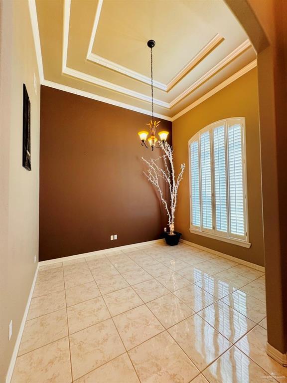 unfurnished dining area with a raised ceiling, crown molding, and an inviting chandelier