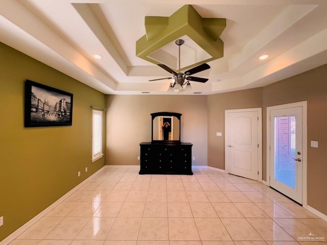 unfurnished bedroom featuring ceiling fan, access to exterior, light tile patterned floors, and a tray ceiling