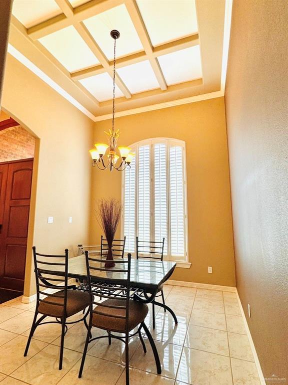 dining area featuring beam ceiling, coffered ceiling, a chandelier, light tile patterned flooring, and ornamental molding