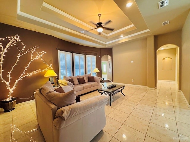 tiled living room featuring a raised ceiling, ceiling fan, and crown molding