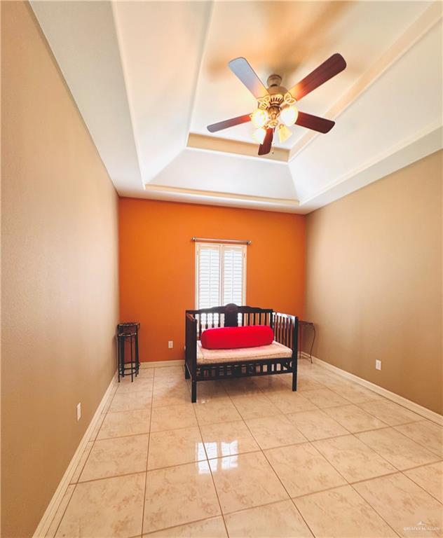 bedroom featuring ceiling fan, light tile patterned floors, and a tray ceiling