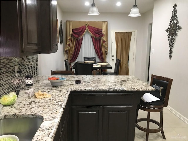 kitchen featuring a peninsula, light stone countertops, baseboards, and decorative backsplash