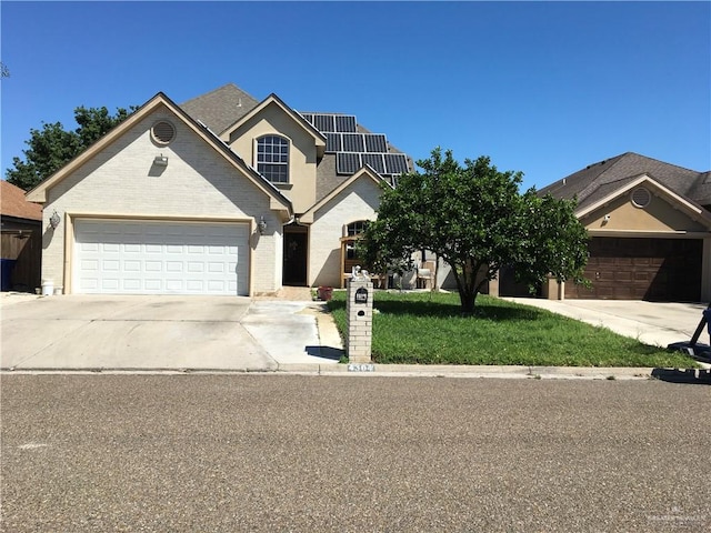 view of front of home with a garage, concrete driveway, roof mounted solar panels, a front lawn, and brick siding