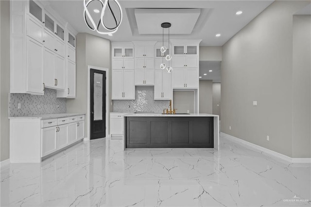 kitchen featuring backsplash, a kitchen island with sink, hanging light fixtures, and white cabinets