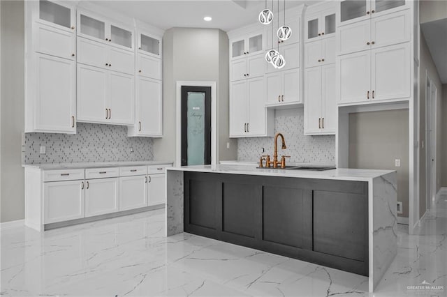 kitchen featuring tasteful backsplash, an island with sink, sink, white cabinets, and hanging light fixtures