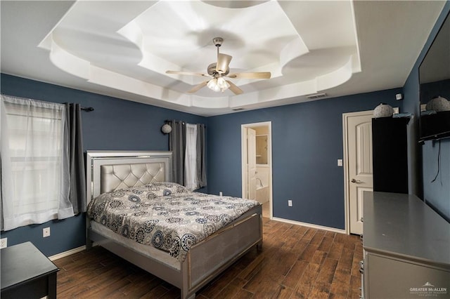 bedroom featuring a raised ceiling, ensuite bath, ceiling fan, and dark hardwood / wood-style flooring