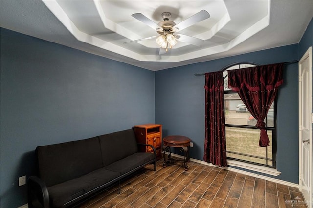 living area featuring dark hardwood / wood-style floors, ceiling fan, and a raised ceiling