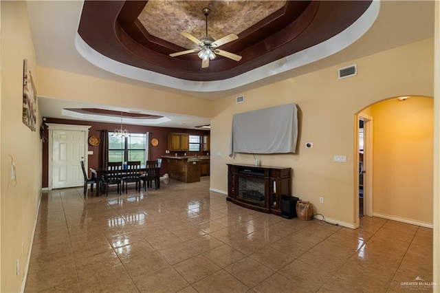 living room with a raised ceiling, tile patterned floors, and ceiling fan with notable chandelier