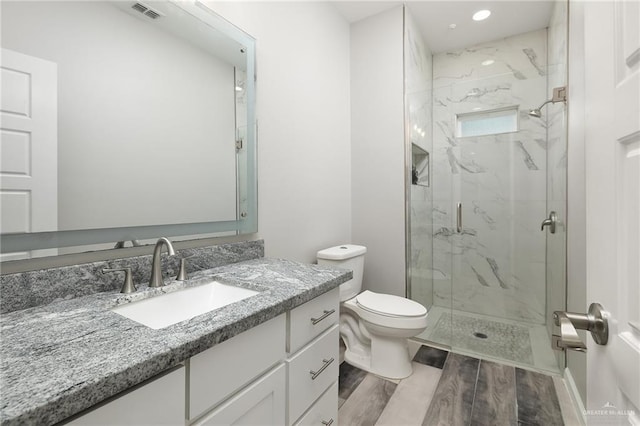 bathroom featuring toilet, wood finished floors, vanity, visible vents, and a marble finish shower